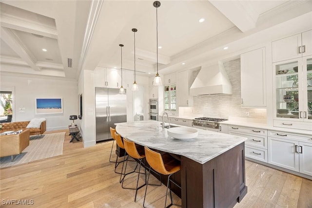 kitchen with premium range hood, white cabinetry, stainless steel appliances, and an island with sink