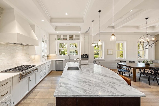 kitchen featuring stainless steel appliances, a center island with sink, white cabinetry, and premium range hood