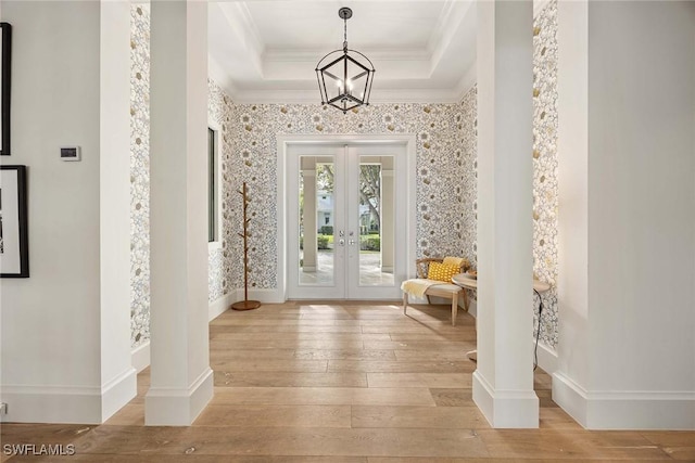 foyer with french doors, a raised ceiling, crown molding, light hardwood / wood-style flooring, and a notable chandelier