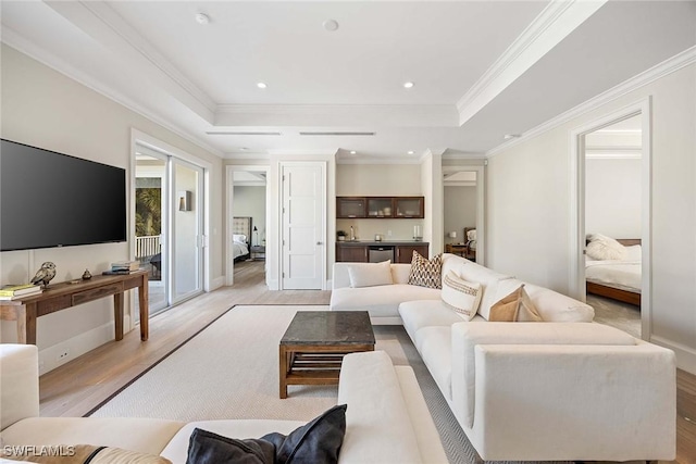 living room featuring a raised ceiling, light wood-type flooring, and ornamental molding