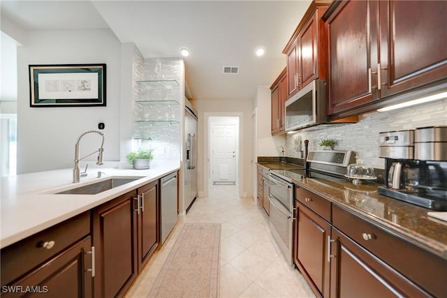 kitchen with sink, decorative backsplash, dark stone countertops, light tile patterned floors, and appliances with stainless steel finishes