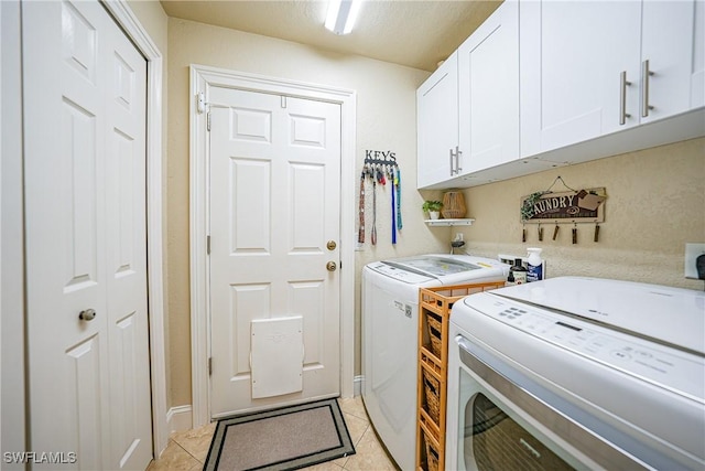 clothes washing area with separate washer and dryer, light tile patterned floors, and cabinets