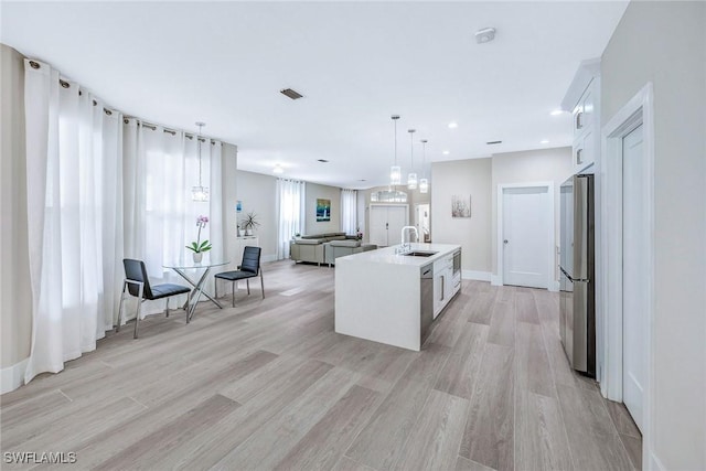 kitchen with stainless steel refrigerator, white cabinetry, sink, and a kitchen island with sink