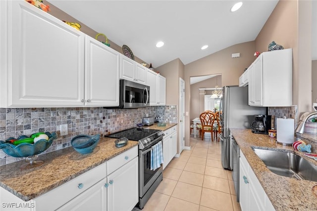 kitchen featuring light stone counters, white cabinets, stainless steel appliances, and lofted ceiling