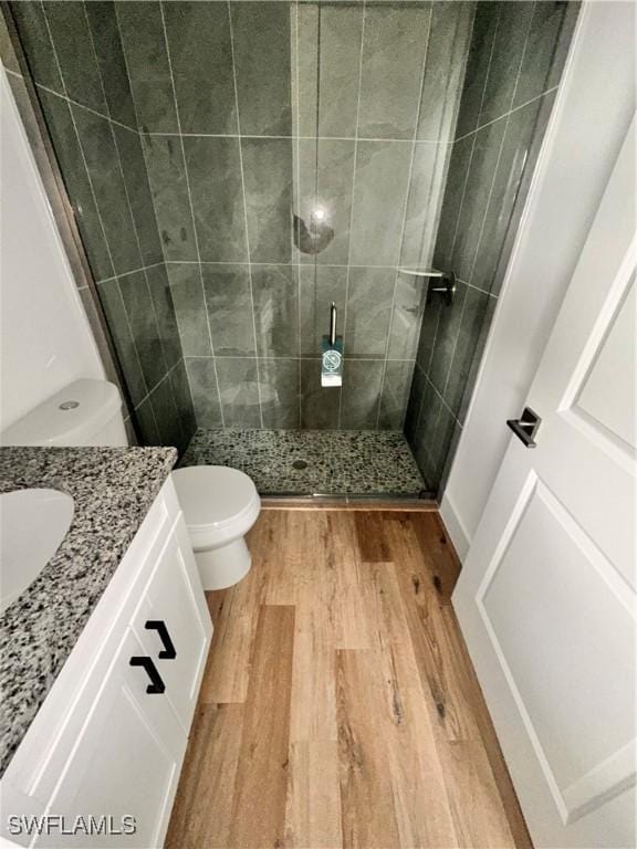 bathroom featuring vanity, toilet, a tile shower, and wood-type flooring