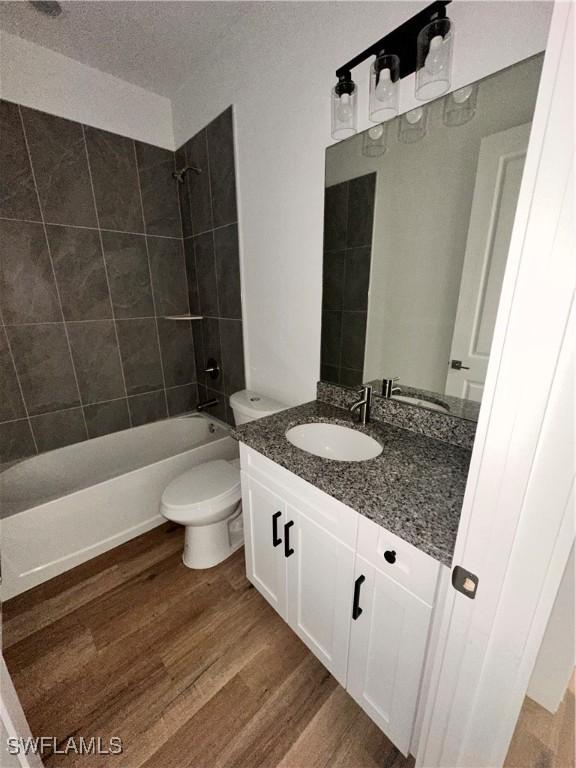 full bathroom featuring vanity, hardwood / wood-style floors, tiled shower / bath combo, and toilet