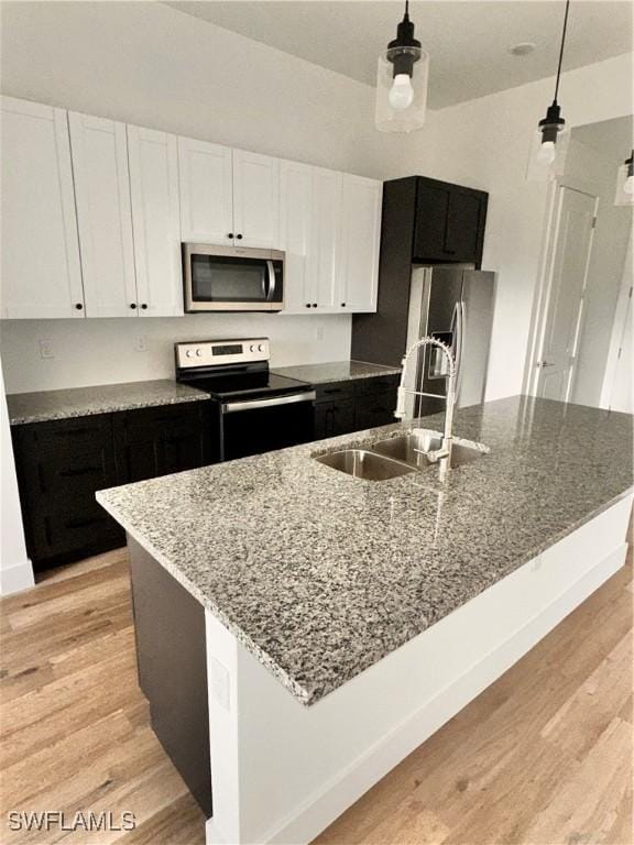 kitchen featuring a kitchen island with sink, sink, stainless steel appliances, and hanging light fixtures