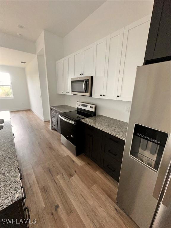 kitchen featuring white cabinets, light stone counters, stainless steel appliances, and light hardwood / wood-style flooring