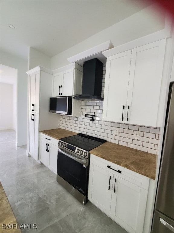 kitchen with wall chimney exhaust hood, decorative backsplash, white cabinetry, and appliances with stainless steel finishes