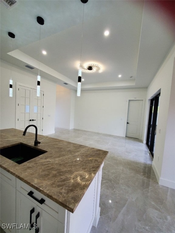 kitchen featuring decorative light fixtures, white cabinetry, sink, and a tray ceiling