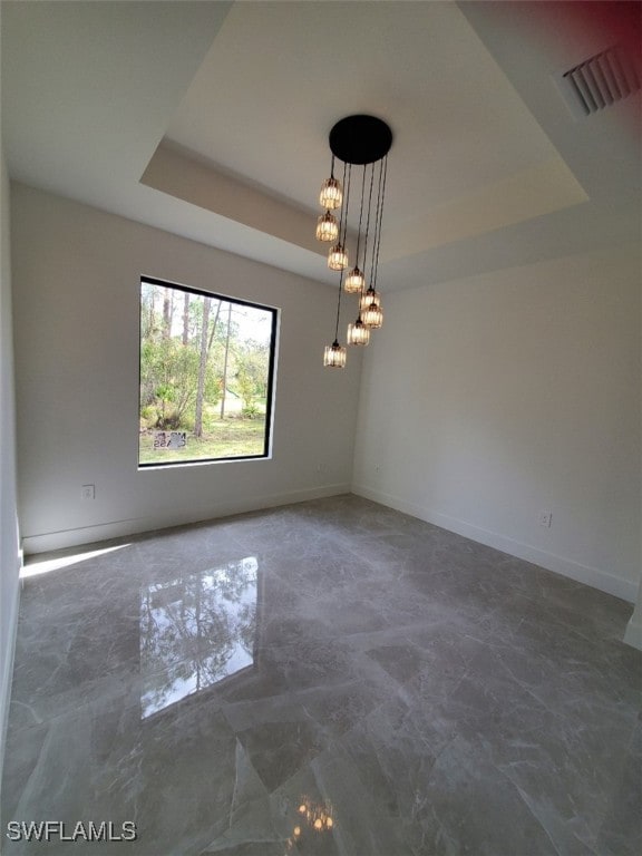 empty room with a raised ceiling and a notable chandelier