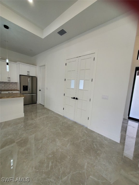 interior space with white cabinetry, a raised ceiling, stainless steel refrigerator with ice dispenser, decorative light fixtures, and decorative backsplash