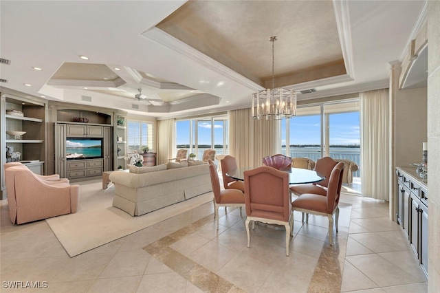 dining room with a raised ceiling, ceiling fan with notable chandelier, a water view, and crown molding