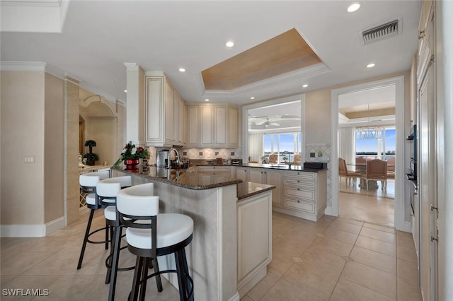 kitchen with cream cabinets, visible vents, a kitchen breakfast bar, ornamental molding, and a raised ceiling