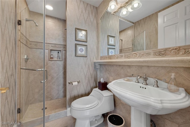 full bath featuring a sink, a shower stall, toilet, and tile walls