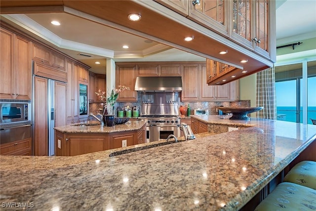 kitchen featuring a kitchen island, sink, built in appliances, a water view, and light stone countertops