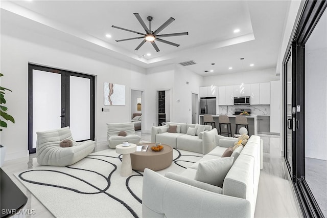 living room with ceiling fan, a raised ceiling, a high ceiling, and french doors