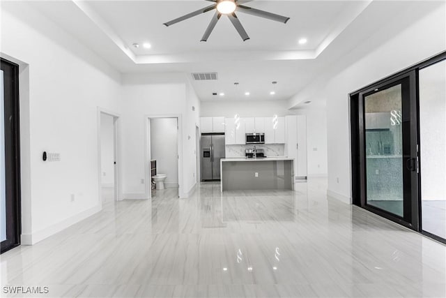 unfurnished living room featuring a raised ceiling and ceiling fan