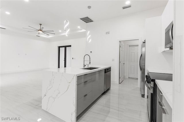 kitchen with gray cabinetry, a kitchen island with sink, sink, ceiling fan, and stainless steel appliances