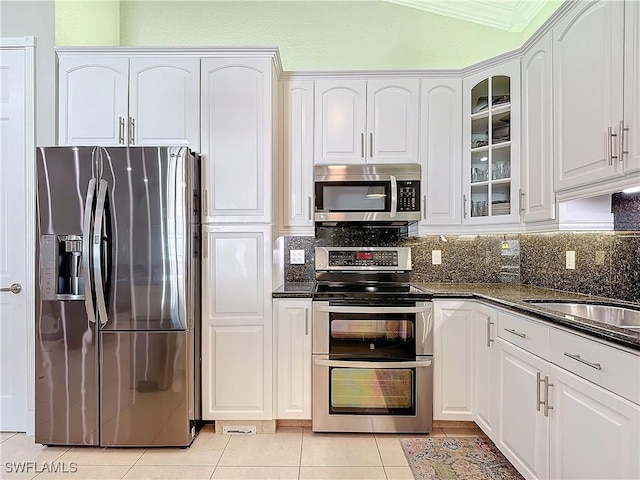 kitchen featuring light tile patterned floors, dark stone countertops, stainless steel appliances, tasteful backsplash, and white cabinets