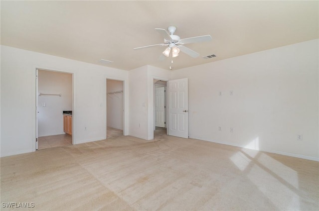 unfurnished bedroom featuring ensuite bath, a spacious closet, ceiling fan, light colored carpet, and a closet