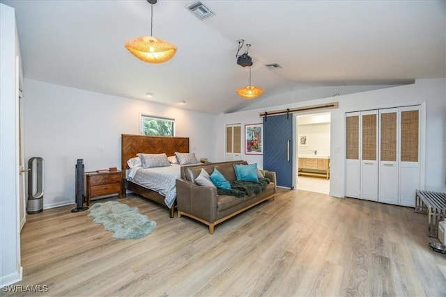 bedroom featuring lofted ceiling, a barn door, light hardwood / wood-style floors, and ensuite bathroom