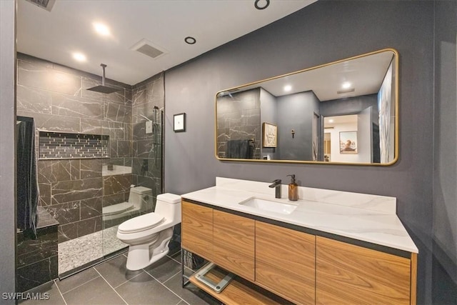 bathroom with tile patterned flooring, vanity, toilet, and tiled shower