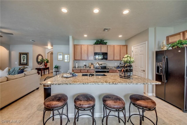 kitchen featuring light brown cabinetry, sink, a kitchen island with sink, and black appliances