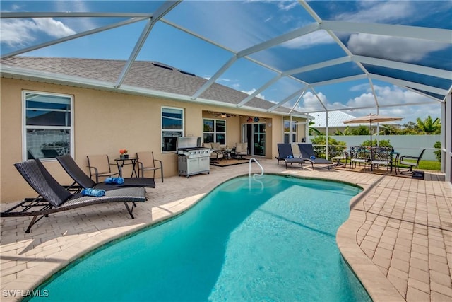 view of pool with glass enclosure, grilling area, and a patio area