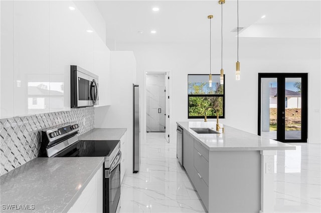 kitchen with stainless steel appliances, a kitchen island with sink, sink, white cabinets, and hanging light fixtures