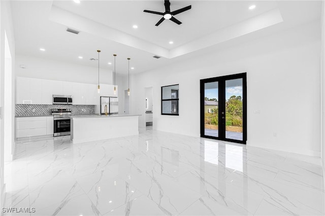 unfurnished living room with french doors, a tray ceiling, and ceiling fan