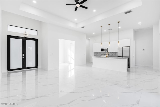 kitchen featuring stainless steel appliances, a raised ceiling, white cabinets, hanging light fixtures, and an island with sink