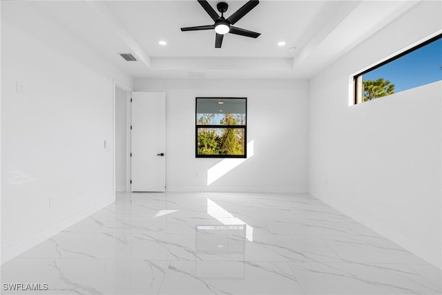 empty room with ceiling fan and a tray ceiling