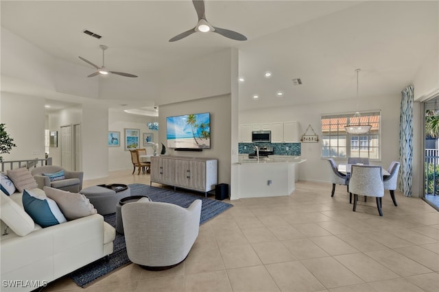 tiled living room with a high ceiling and ceiling fan with notable chandelier