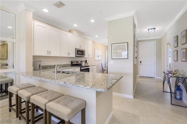 kitchen featuring kitchen peninsula, sink, appliances with stainless steel finishes, a kitchen bar, and white cabinetry