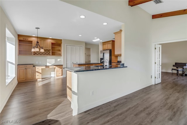 kitchen with dark stone countertops, wood-type flooring, stainless steel fridge with ice dispenser, kitchen peninsula, and hanging light fixtures