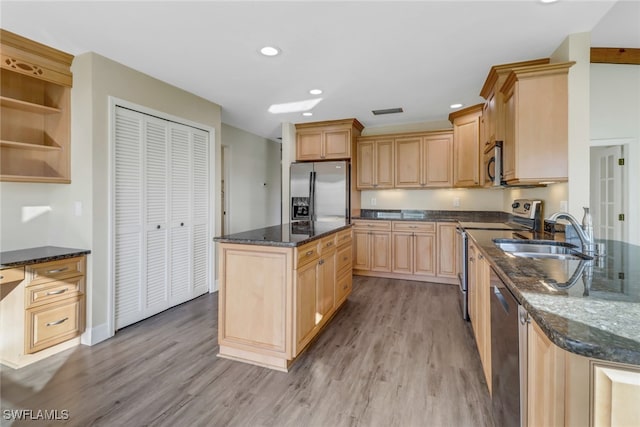 kitchen featuring appliances with stainless steel finishes, sink, light wood-type flooring, dark stone counters, and light brown cabinetry