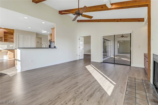 unfurnished living room with ceiling fan, sink, hardwood / wood-style floors, and lofted ceiling with beams