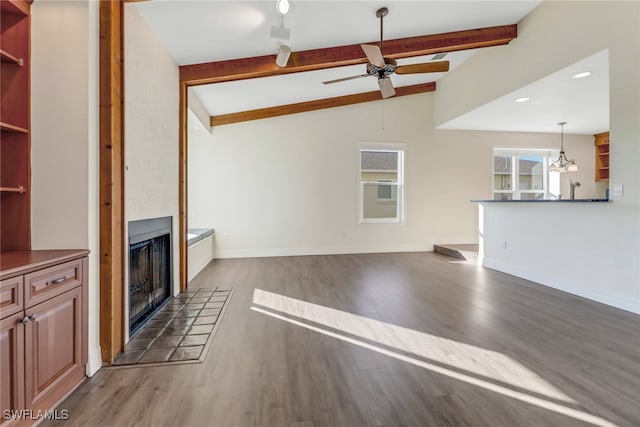 unfurnished living room featuring ceiling fan, a tiled fireplace, vaulted ceiling with beams, and dark wood-type flooring