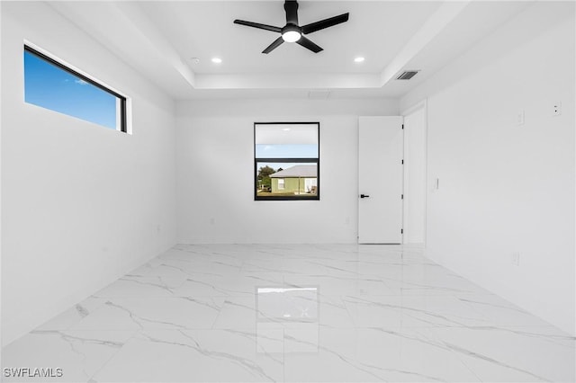 empty room with ceiling fan and a raised ceiling