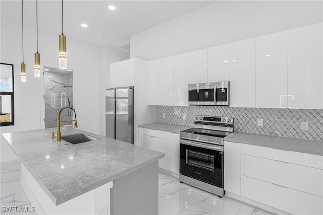 kitchen featuring pendant lighting, a kitchen island with sink, sink, appliances with stainless steel finishes, and white cabinetry