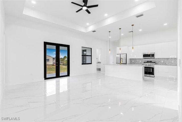 unfurnished living room featuring a tray ceiling, ceiling fan, and french doors