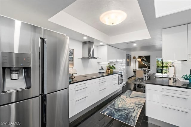 kitchen with stainless steel appliances, white cabinets, wall chimney range hood, a raised ceiling, and sink