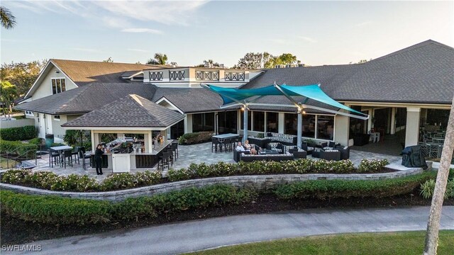 back house at dusk with a patio area, an outdoor living space, and exterior bar