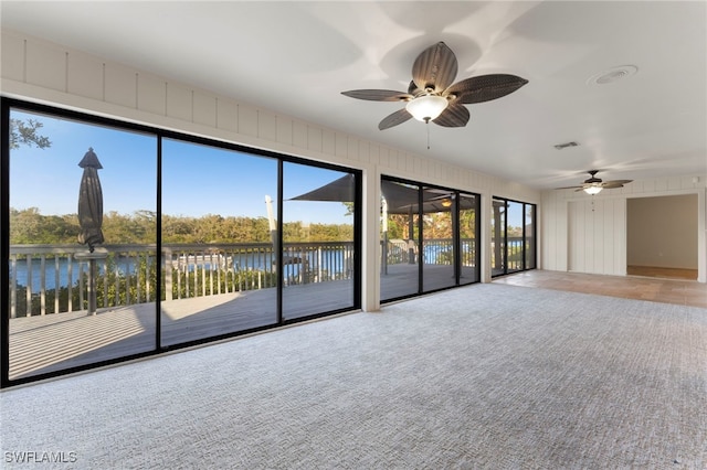 carpeted empty room featuring ceiling fan and a water view