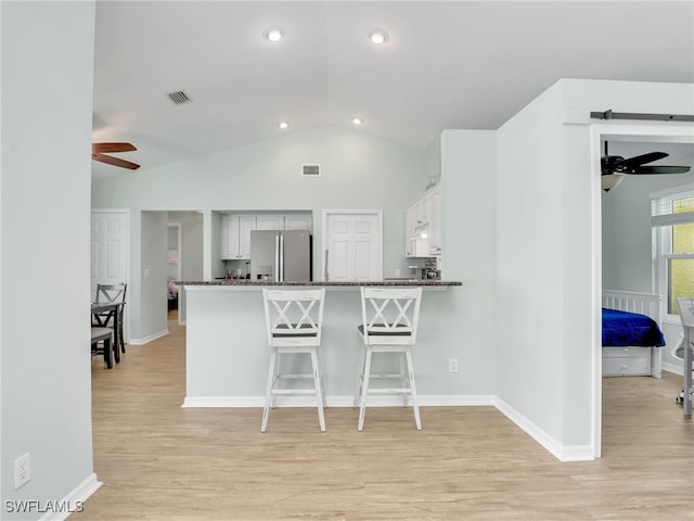 kitchen with stainless steel fridge with ice dispenser, kitchen peninsula, dark stone counters, a breakfast bar area, and white cabinets