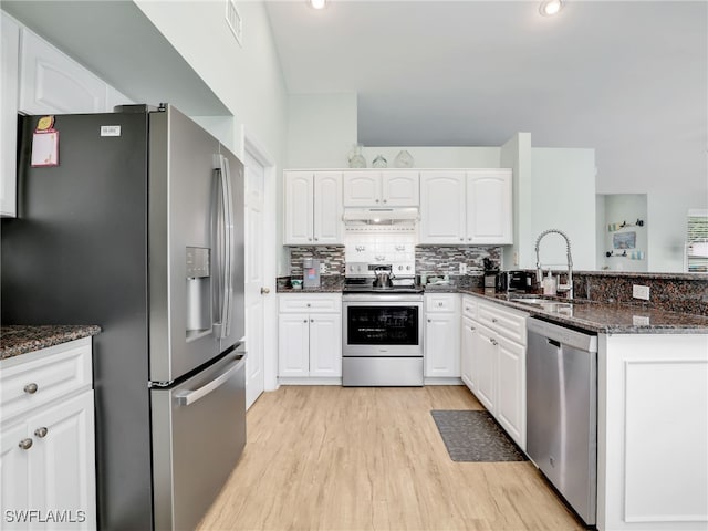 kitchen featuring appliances with stainless steel finishes, dark stone counters, sink, light hardwood / wood-style flooring, and white cabinets