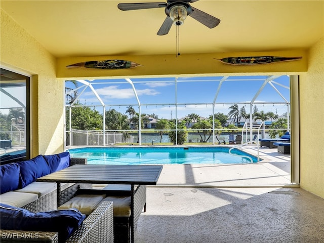 view of swimming pool featuring outdoor lounge area, ceiling fan, a water view, glass enclosure, and a patio area