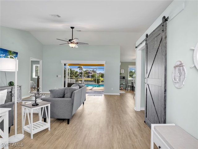 living room featuring ceiling fan, a barn door, light hardwood / wood-style floors, and vaulted ceiling