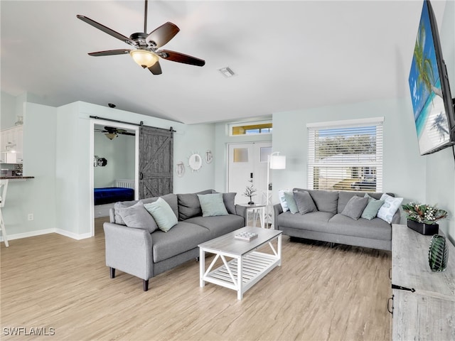 living room with light wood-type flooring, a barn door, and ceiling fan